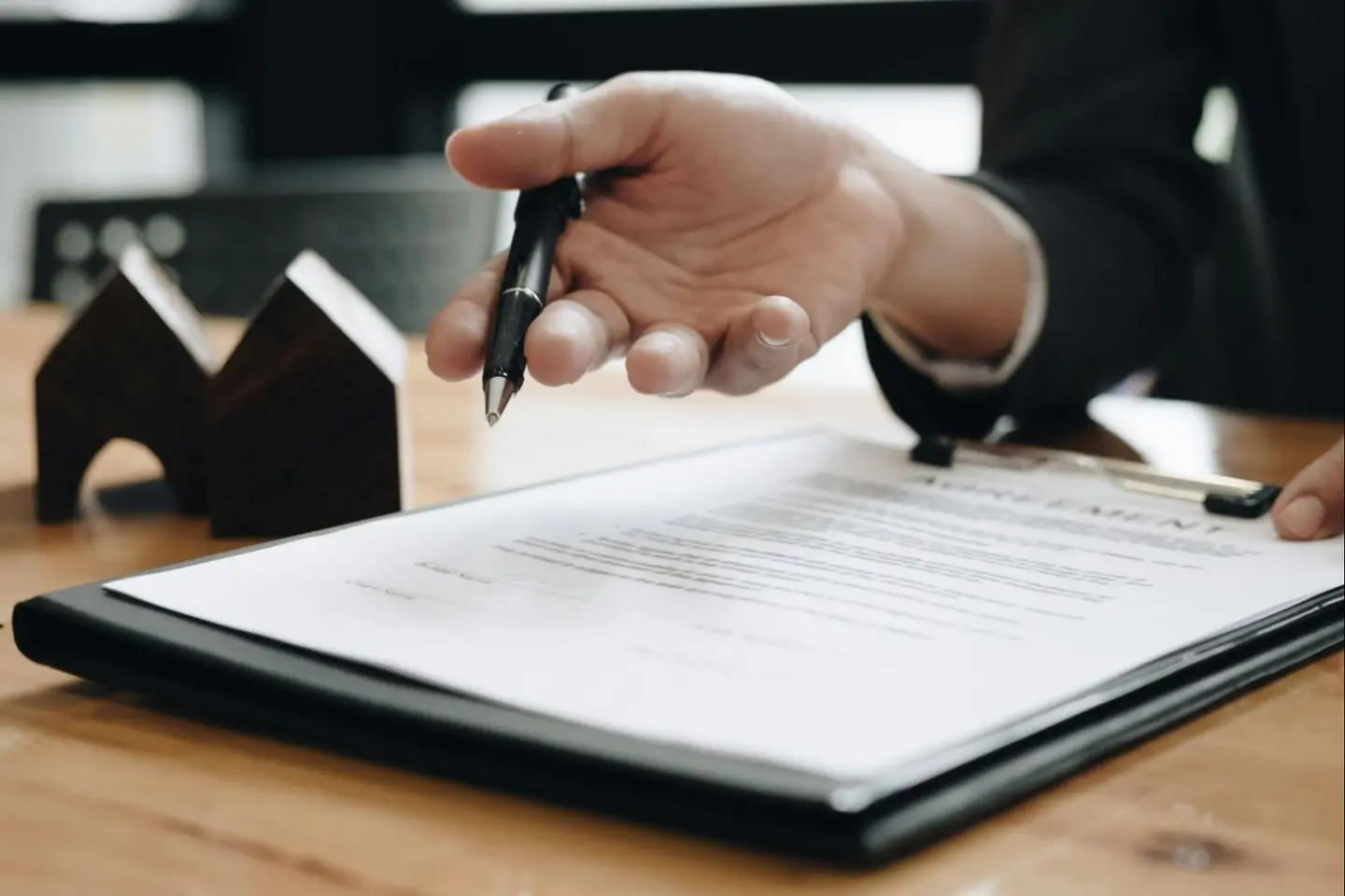 A hand signing paperwork beside a small model house